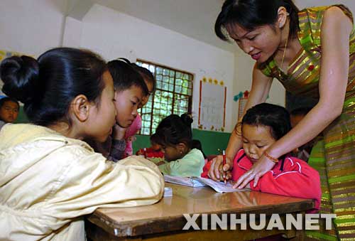 2004年12月3日，云南省西雙版納傣族自治州景洪市勐罕鎮(zhèn)曼聽村的黨員、教師玉罕約（右一）在給村小學(xué)的孩子們補(bǔ)習(xí)功課。曼聽村是一個(gè)典型的傣族村寨，近兩年來，曼聽村黨支部大力加強(qiáng)基層黨組織建設(shè)，村黨支部充分發(fā)揮黨員在經(jīng)濟(jì)建設(shè)中的作用，帶領(lǐng)群眾學(xué)科技、調(diào)結(jié)構(gòu)、闖市場(chǎng)，開辦科技講座和黨課培訓(xùn)，使得村里經(jīng)濟(jì)發(fā)展迅速，人民生活明顯改善。 新華社發(fā) 