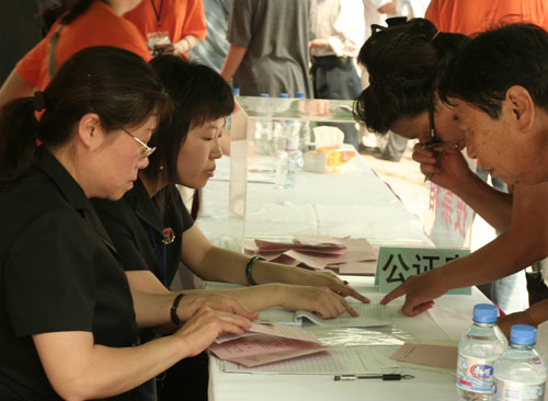 Two notary officials check the documents of voters at the venue for a vote on demolishment and reconstruction of old buildings in Juixiaqiao Sub-district in Beijing, June 9, 2007. Local government and the real estate developer jointly organize the vote on Saturday to see if majority residents of over 5000 families accept the new compensation policy after failed attempts to reach an agreement through other ways. Both notary officials and supervisors are invited to monitor the vote that runs from 9 a.m. to 9 p.m. at six ballot booths. [Sun Yuqing/www.hwdly.com.cn]